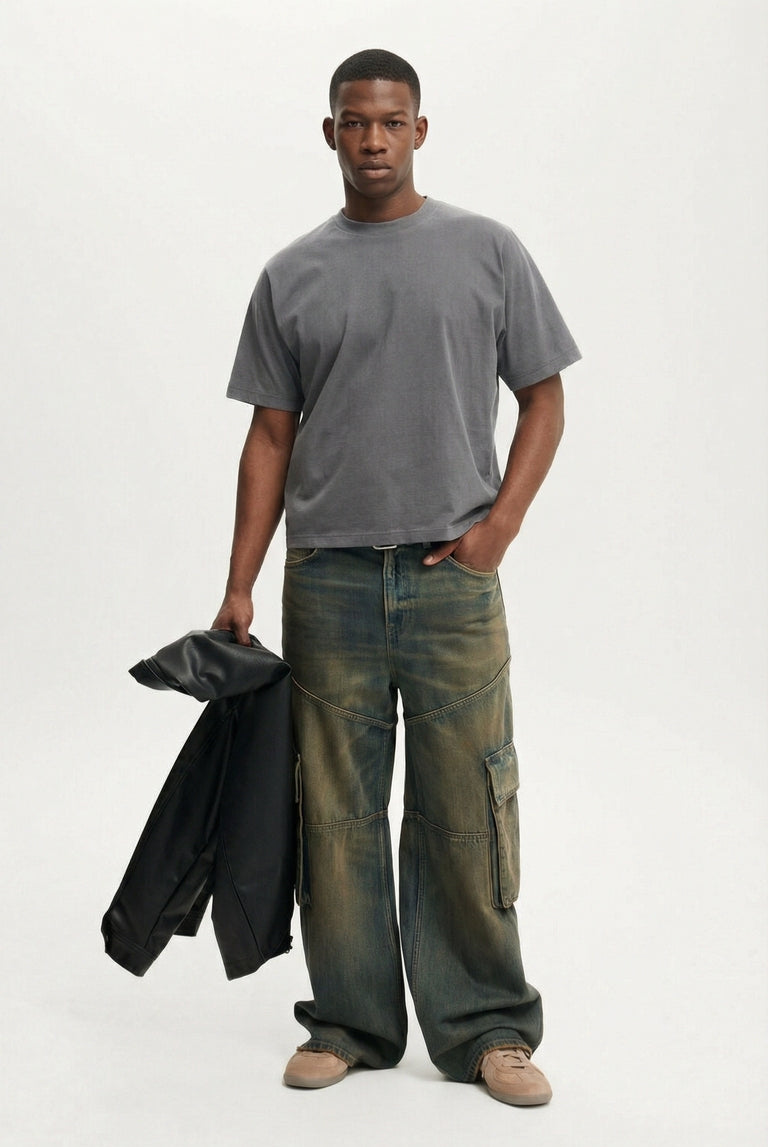 Man wearing a gray t-shirt and green cargo pants holding a black jacket on a white background